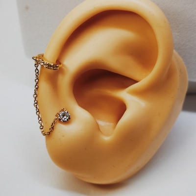 Brincos dourados com corrente e pedra brilhante em orelha artificial bege