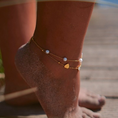 Pé com tornozeleira dourada com contas brancas e coração amarelo ao ar livre