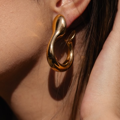 Brinco dourado pendente com design curvo na orelha de uma pessoa.
