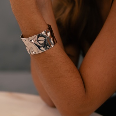 Pulseira metálica prateada larga e texturizada no pulso de uma pessoa