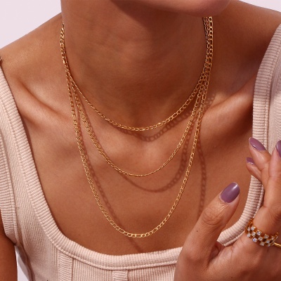 Colar dourado de três camadas em modelo com camisola bege e anéis dourados.