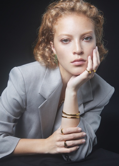 Mulher com casaco cinzento claro e joias douradas e verdes