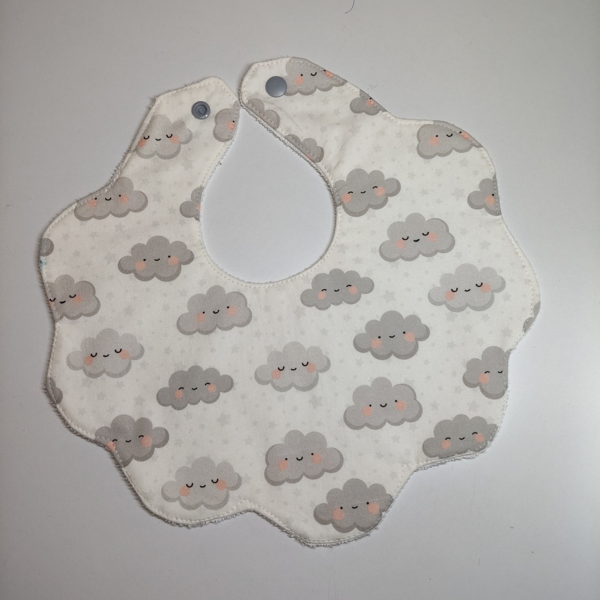 Babete para bebé em algodão com padrão de nuvens sorridentes em fundo branco