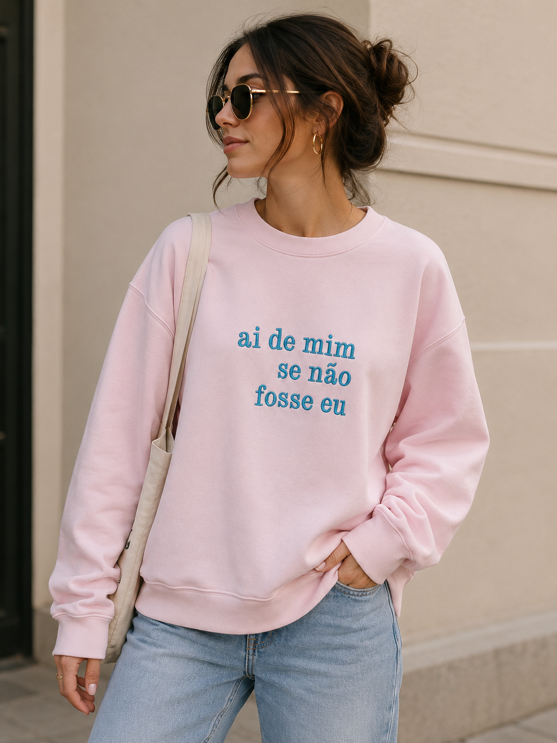 Mulher com sweatshirt rosa claro com texto azul em ambiente urbano claro