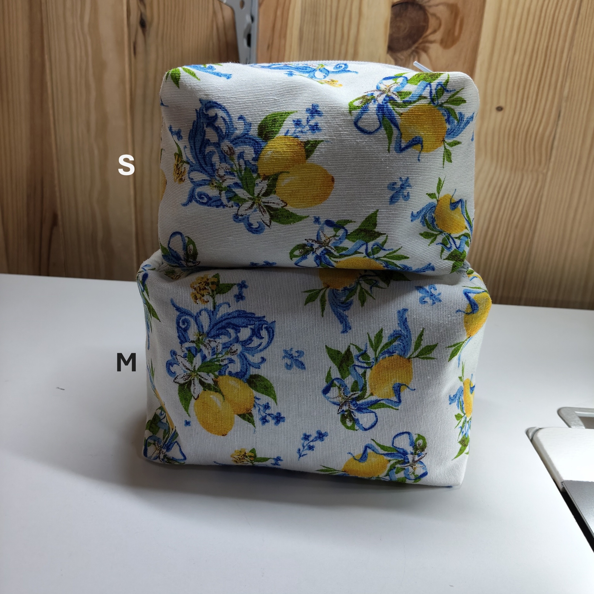 Duas bolsas de tecido com padrão de limões e arabescos azuis sobre fundo branco, empilhadas sobre superfície branca com fundo de madeira.