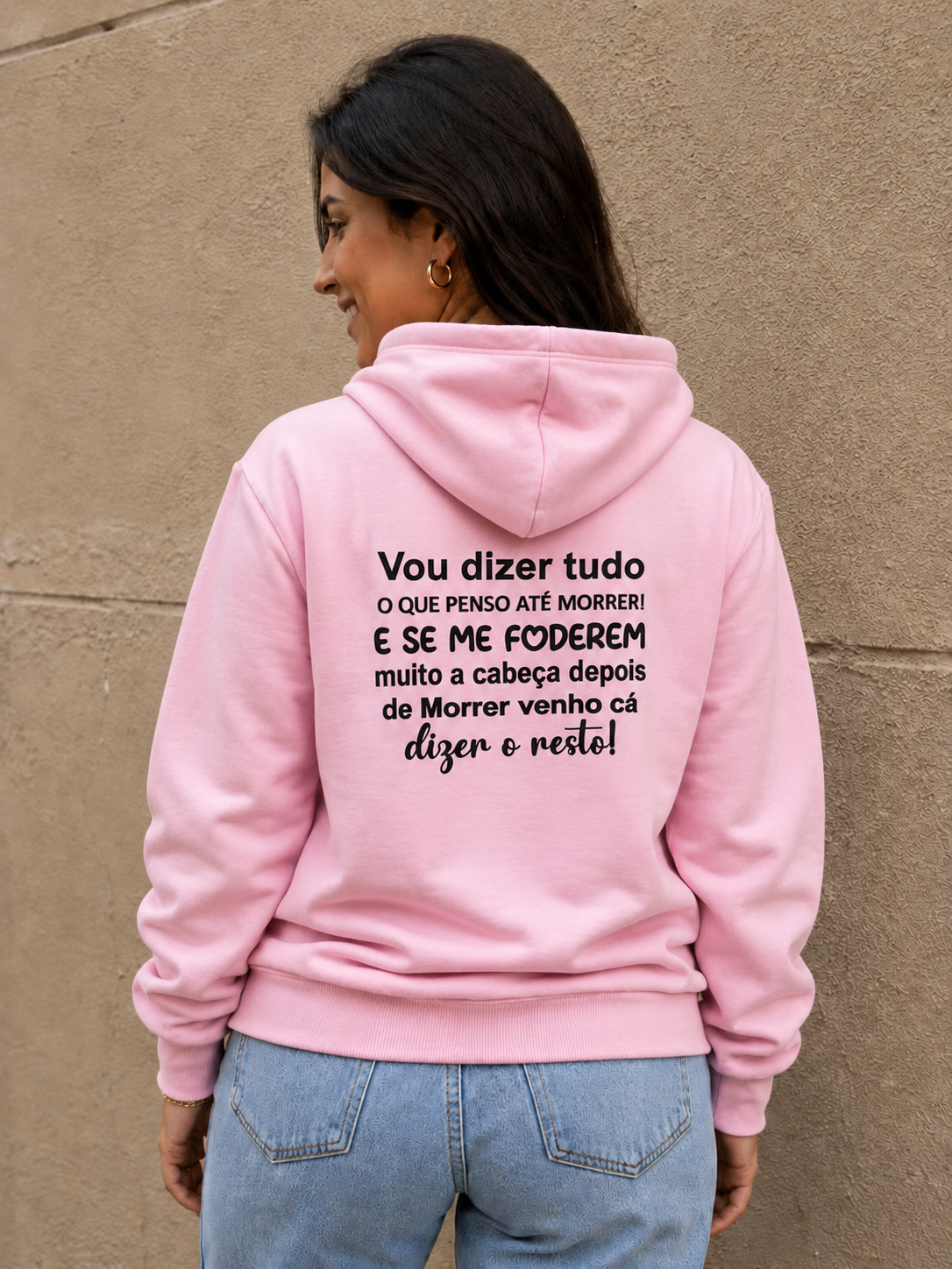Mulher de costas a usar sweatshirt rosa com texto preto nas costas, contra parede bege texturizada
