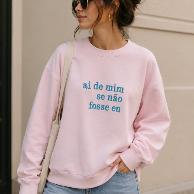 Mulher com sweatshirt rosa claro com texto azul em ambiente urbano claro
