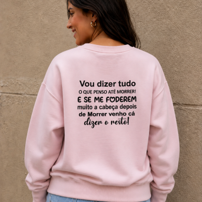 Pessoa com sweatshirt rosa claro com texto em preto nas costas, jeans azuis claros e parede bege de fundo.