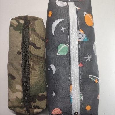 Duas bolsas retangulares, uma camuflada e outra com padrão espacial, fechadas com zíper