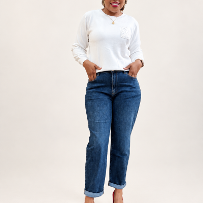 Mulher com camisola branca, jeans azuis e sapatos vermelhos, em fundo neutro.