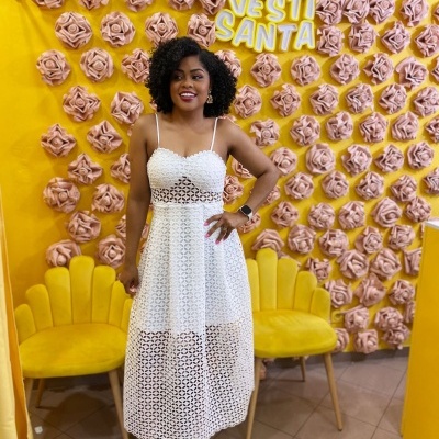 Mulher com vestido branco em fundo amarelo decorado com flores e cadeiras amarelas