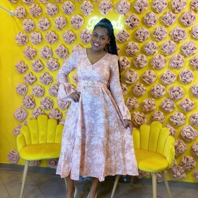 Mulher a usar vestido rosa claro com padrão floral branco e sapatos brancos em background amarelo com flores e cadeiras amarelas