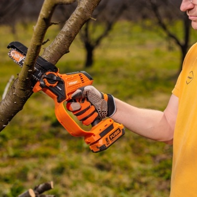 Motosserra laranja da marca Villager a cortar ramo de árvore com pessoa a usar polo amarelo e luvas