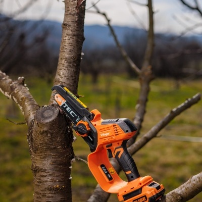 Mini motosserra elétrica portátil laranja e preta em ramo de árvore