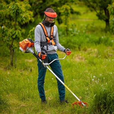 Pessoa com equipamento de proteção a operar desbrossadora num campo verde