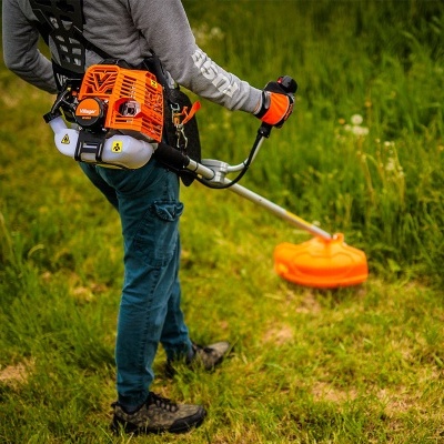 Homem usando roçadora de relva laranja e prata com motor mochila Villager em campo verde