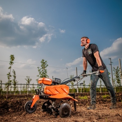 Homem com motocultivadora Villager alaranjada em campo de terra arada sob céu azul