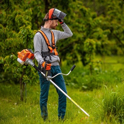 Homem a usar aparador de relva motorizado num campo verde