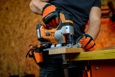 Serra tico-tico laranja e preto a cortar madeira numa bancada amarela