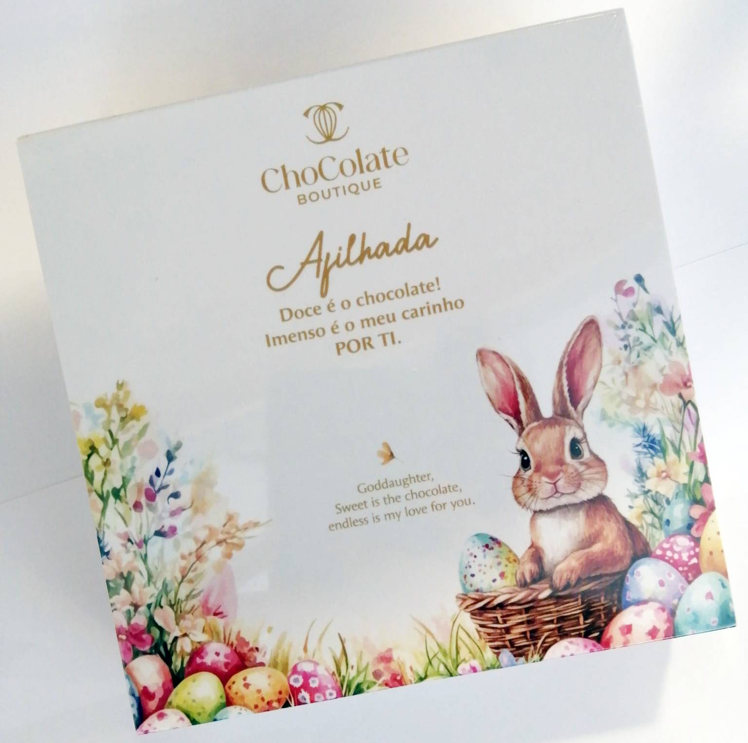 Maria Chocolate Caixa 9 Bombons Afilhada Chocolate Fabrico Artesanal Caixa branca de chocolate com coelho, ovos coloridos e texto em dourado e castanho