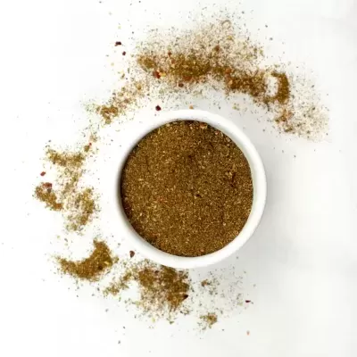 Recipiente branco com especiarias em pó castanho esverdeadas e partículas vermelhas espalhadas