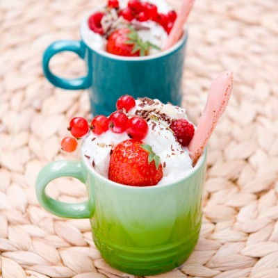 Dois copos coloridos com chantilly e frutas vermelhas em base de palha