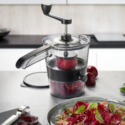 Triturador manual transparente com alavanca preta e beterraba no interior sobre bancada de cozinha clara