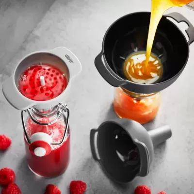 Funis de plástico a verter líquido em garrafas de vidro com framboesas ao redor