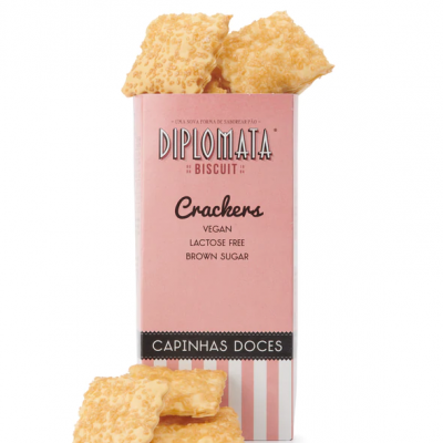 Pacote rosa com riscas brancas dos crackers Diplomata Biscuit e quatro crackers quadrados dourados crocantes.