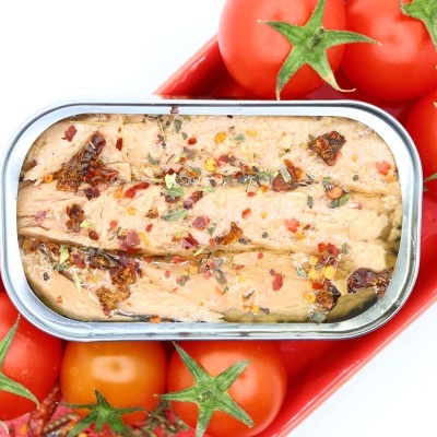 Lata aberta de conserva de peixe com pedaços de tomate seco sobre bandeja vermelha com tomates frescos