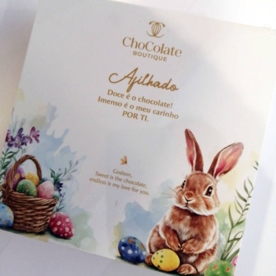 Embalagem branca com texto dourado, coelho e ovos de Páscoa coloridos.