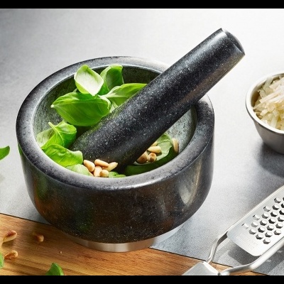 Pilão de pedra com folhas e pinhões, ralador, queijo ralado e recipiente com pinhões