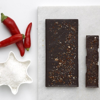 Barra de chocolate preto com pimenta e sal grosso, pimentas vermelhas e recipiente branco com sal grosso
