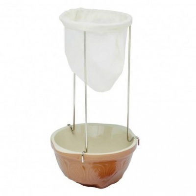 Filtro de café manual com suporte metálico, saco de tecido branco e jarra de cerâmica bege.