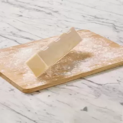 Barra de chocolate branco em tábua de madeira polvilhada com farinha sobre superfície branca marmorizada