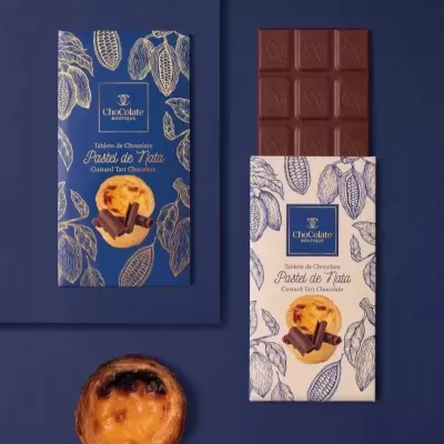 Duas embalagens de chocolate ChoColate Boutique e pastel de nata sobre fundo azul