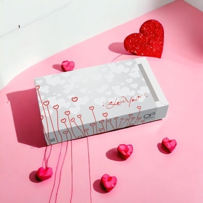 Caixa branca decorada com corações vermelhos e frase Love You, com corações decorativos rosa e vermelho num fundo rosa