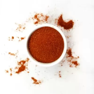 Tigela branca com pó vermelho e pó espalhado à volta sobre superfície branca