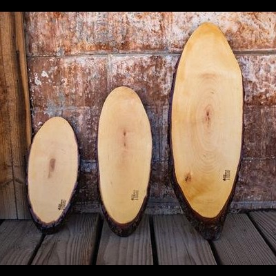 Três tábuas ovaladas de madeira natural contra parede rústica.