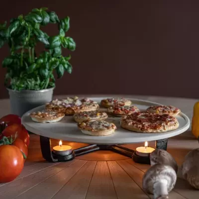 Suporte metálico com mini pizzas e velas acesas, rodeado de legumes e planta