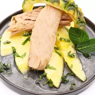 Prato preto com fatias de abacaxi, atum em conserva e folhas verdes