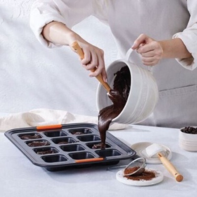 Pessoa a verter massa de chocolate em formas de silicone num tabuleiro para bolos