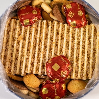 Caixa metálica aberta com bolachas rectangulares, bolachas redondas embaladas em papel vermelho com dourado e outras bolachas variadas