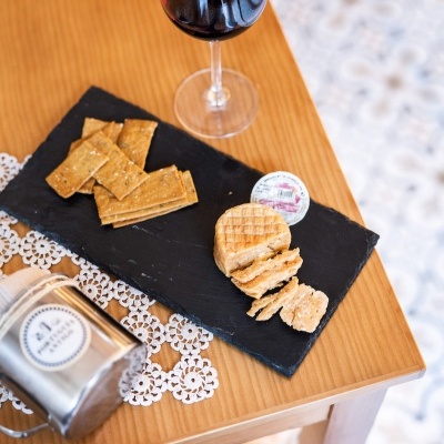 Mesa de madeira com prato preto contendo bolachas integrais e taça de vinho tinto.