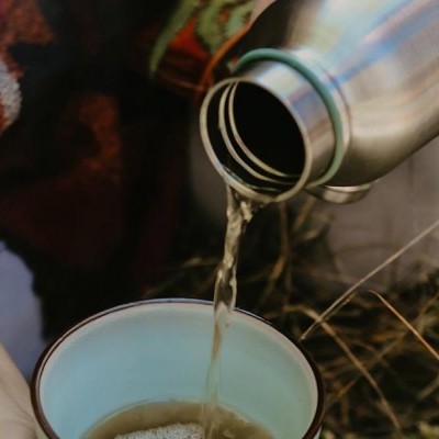 Garrafa térmica a despejar líquído em caneca azul ao ar livre