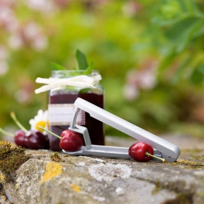 Dispositivo para remover caroços de cerejas ao lado de frasco de compota num jardim