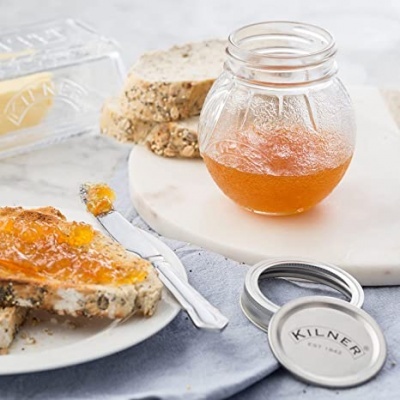 Frasco de vidro com geleia e pão multicereais sobre prato e tábua branca