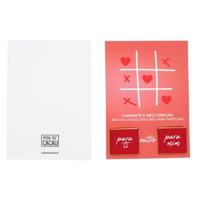 Conjunto de chocolates em cartão vermelho com jogo da velha e texto, acompanhado de cartão branco com logo PEDAÇOS DE CACAU.