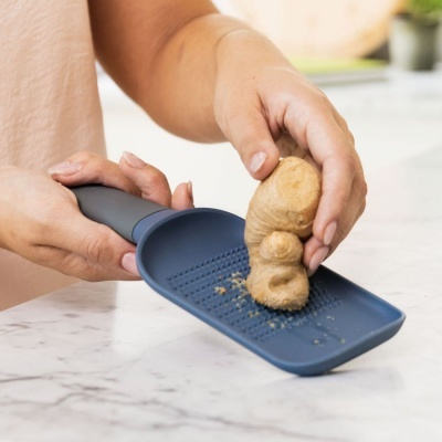 Ralador azul com gengibre a ser usado numa bancada de cozinha