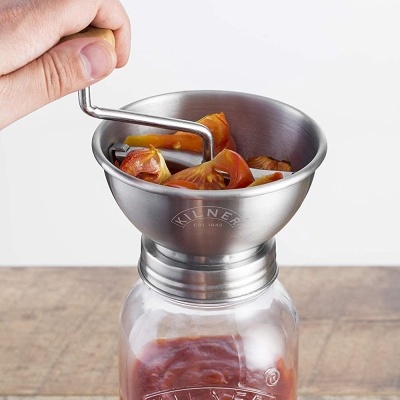 Frasco Kilner a ser enchido com tomate através de funil metálico com pedaços de tomate
